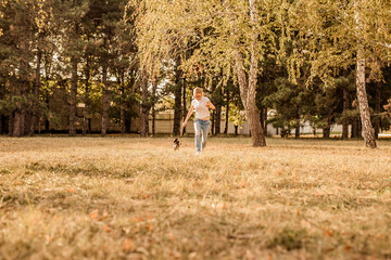 Teenager blonde girl with big glasses laughing and playing with little puppy spaniel in the warm park