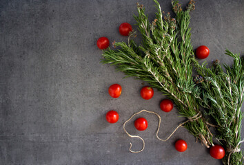 Rosemary bounds and cherry tomatoes on dark grey textured background. Top view photo of fresh...