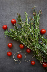 Rosemary bounds and cherry tomatoes on dark grey textured background. Top view photo of fresh...