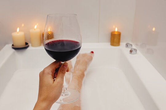 Woman drinking red wine while taking bath with foam