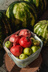 Harvest of green apples, watermelons and pomegranates in a stylish white basket.