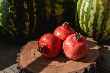 Ripe three pomegranates on a wooden round board, in the background watermelons. Harvesting concept. Sale of fruits.