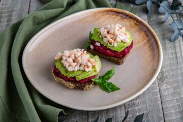 Corn bread bruschetta with avocado and shrimp on a beetroot pillow. A healthy, nutritious snack. Healthy breakfast. Still life in gray-green shades.