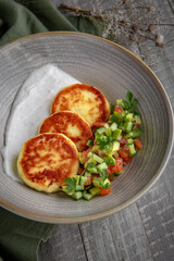 Unsweetened cottage cheese pancakes with sour cream and cucumber salad with stomata. Healthy breakfast. Still life in gray-green shades.