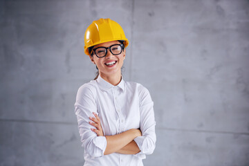 Smiling young female architect with helmet on head standing with arms crossed.
