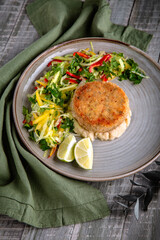 Crab cutlet on a pillow of celery puree with a salad of fresh vegetables and herbs. Delicious, healthy, nutritious dietary meal. Still life in gray-green shades.