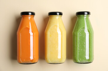 Bottles with delicious colorful juices on beige background, flat lay