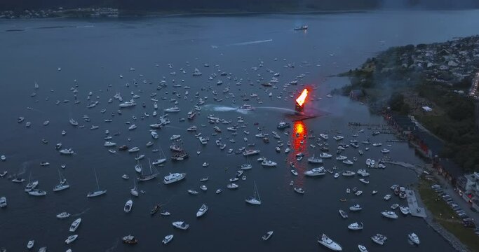 Unbelievably picturesque, cinematic, high altitude, approaching aerial footage that reveals the biggest bonfire event on Earth and the small boats gathering around it near Alesund, Norway at dusk.