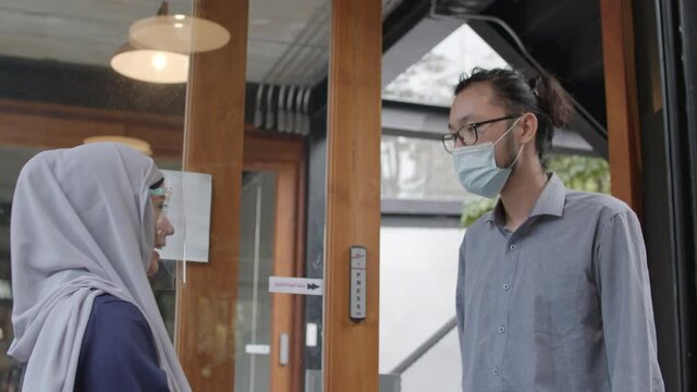 Asian staff Muslim woman standing at door to measure a fever customer before interring into the shop during protecting Coronavirus or covid 19 in Thailand
