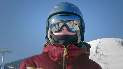 A beautiful girl puts on winter goggles or a mask for snowboarding. The concept of victory in sports, winning, win. Getting ready for skiing on a snowy slope. Winter travel at the ski resort.