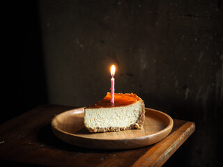 plain cheesecake with lighted pink candle on wooden plate