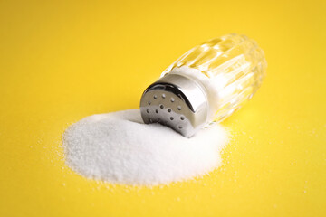 Scattered salt and shaker on yellow background, closeup
