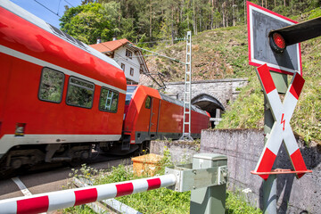 Regionalzug am Bahnübergang mit Schranke und Blinklicht in ländlicher Umgebung
