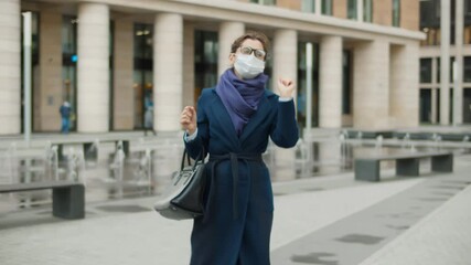 Excited young female entrepreneur wearing safety mask celebrating promotion dancing outdoors