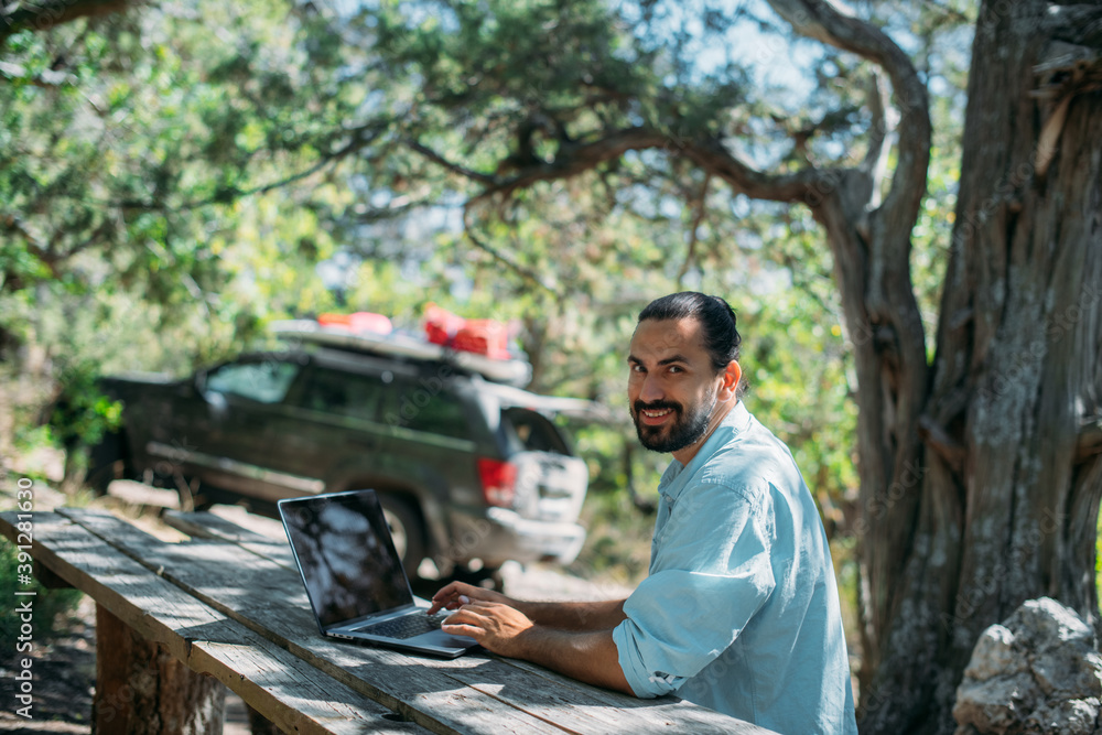 Wall mural Male tourist working on a laptop outdoors in a camping.