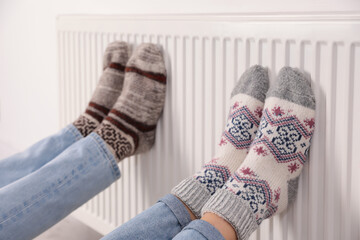 Couple warming legs on heating radiator indoors, closeup