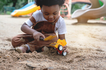 Dark-skinned boy enjoy playing with toy cars and sand at playground