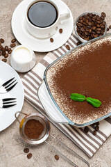 Traditional Italian Tiramisu dessert in glass baking dish and cup of fresh hot espresso coffee on concrete background
