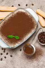Traditional Italian Tiramisu dessert in glass baking dish and savoiardi cookies on concrete background