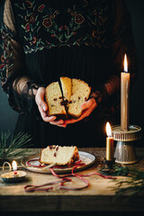 Woman in black dress holding slices of homemade Italian Christmas panettone above old wooden table with lit candles.