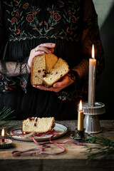 Woman in black dress holding slices of homemade Italian Christmas panettone above old wooden table with lit candles.