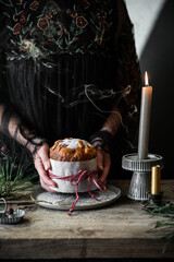 Woman in black dress Holding homemade Italian Christmas panettone above old wooden table with  candles.