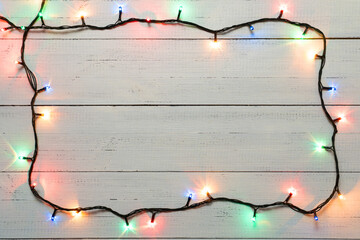 Frame of multicolored electric garland on white wood background, copy space.