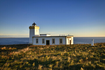 Fototapeta na wymiar Duncansby Head Lighthouse, John O'Groats, Scotland at sunrise with blue sky background and grassy foreground.