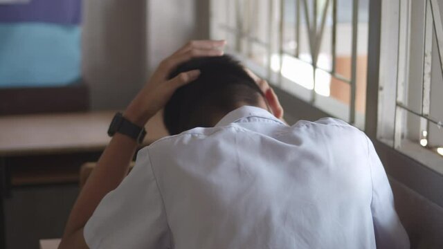 A male high school student in white uniform  is sitting alone, being so tense that he crunched his head in the classroom.
