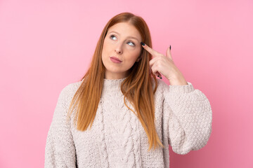 Young redhead woman over isolated pink background making the gesture of madness putting finger on...