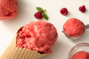 Delicious pink ice cream in wafer cone on white table, closeup