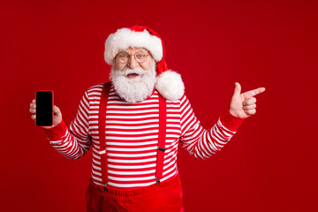 Fototapeta na wymiar Portrait of his he nice handsome glad cheerful bearded Santa holding in hands device demonstrating advert copy space sale like follow isolated bright vivid shine vibrant red color background