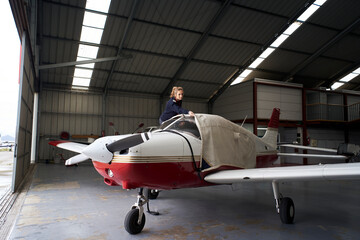 Young female pilot covering light aircraft with protective cover in hangar.
