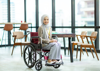 Asian Muslim businesswoman in hijab head scarf sitting on the wheel chair and working in the modern office. businesspeople, diversity and office concept