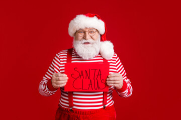 Portrait of his he nice handsome cheerful bearded St Nicholas holding in hands paper card saying words Santa Claus festal event organization isolated bright vivid shine vibrant red color background