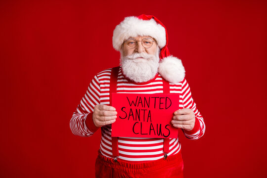 Photo of pensioner grandpa grey beard serious hold paper placard wanted thief stolen present wear santa costume suspenders spectacles striped shirt headwear isolated red color background
