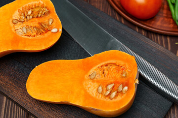 Small pumpkin cut into halves on wooden cutting board with knife