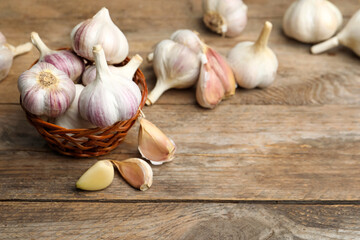 Fresh organic garlic in wicker basket on wooden table. Space for text