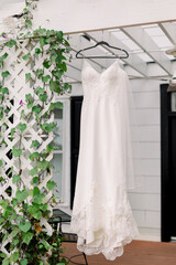 Wedding dress hanging up by a trellis with greenery. 