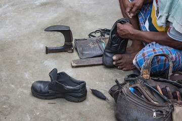Indian local cobbler repairing shoes beside road by hand using tools in traditional way.