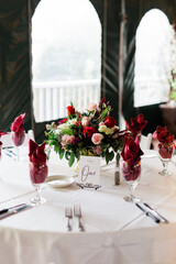 Red napkins in glasses on a table with a beautiful centerpiece with red and pink roses and greenery
