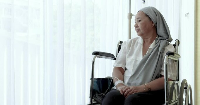 Old Asian woman on a wheel chair looking out and touching the window.