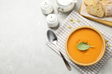 Tasty creamy pumpkin soup with basil in bowl on grey table, flat lay. Space for text