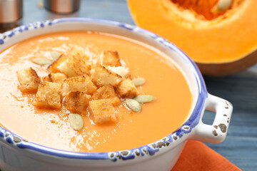 Tasty creamy pumpkin soup with croutons and seeds in bowl on table, closeup