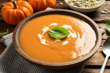 Tasty creamy pumpkin soup with basil in bowl on wooden table