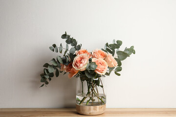 Bouquet with beautiful flowers in glass vase on wooden table against white background