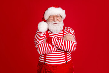 Photo of pensioner old man crossed hands self-assured grandpa listen children christmas wishes wear santa costume suspenders spectacles striped shirt headwear isolated red color background