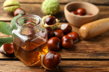 Chestnuts and jar of essential oil on wooden table. Space for text