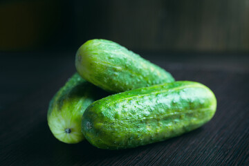 Three ripe cucumbers on a dark wooden background
