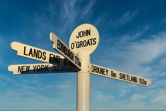 New John O'Groats signpost on NC500 route with blue sky and light cloud background. Mileage to Orkney, Shetland, Lands End, Edinburgh and New York. Famous spot for tourists to get photographs taken.